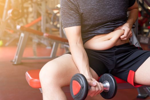 Fat man holding dumbbell and excessive fat belly, overweight fatty belly at fitness gym. Diet lifestyle, weight loss, stomach muscle, healthy concept.