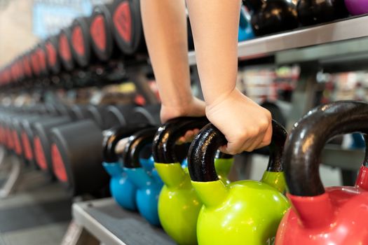 Closeup female hands pick up kettlebell from the set of dumbbell for exercise and strength training. sport, fitness, health, lifestyle and people concept