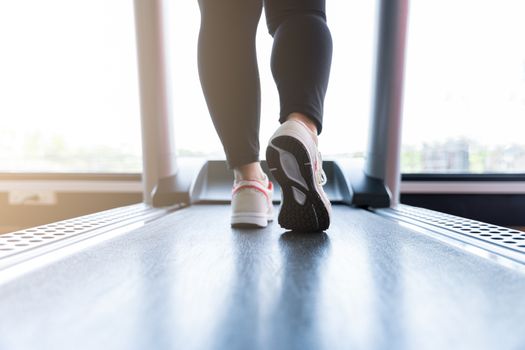 Close up female feet wearing sneakers running on treadmill at fitness gym. Diet lifestyle, weight loss, stomach muscle, healthy concept.