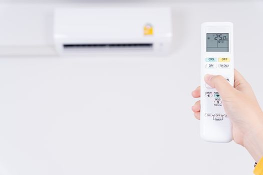 Human hand is using white remote of air conditioner for turn on or adjust temperature of air conditioner inside the room.