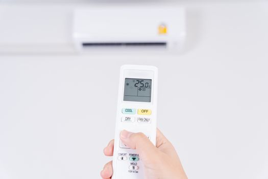 Human hand is using white remote of air conditioner for turn on or adjust temperature of air conditioner inside the room.