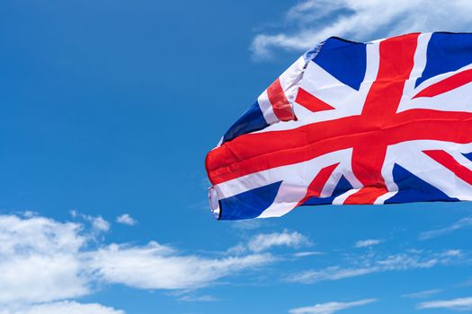 Waving UK flag under blue sky background.