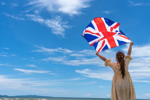 woman standing and holding UK flag under blue sky.