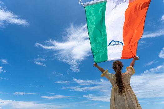 woman standing and holding India flag under blue sky.