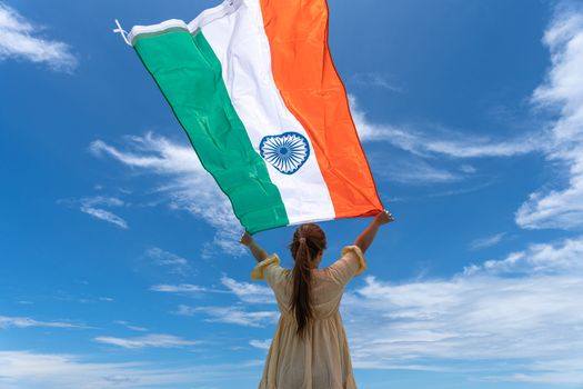 woman standing and holding India flag under blue sky.