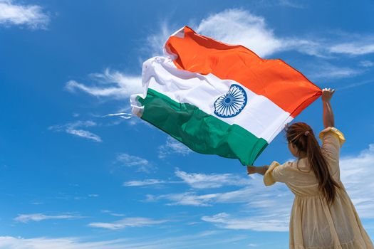 woman standing and holding India flag under blue sky.