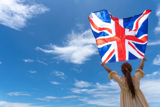 woman standing and holding UK flag under blue sky.