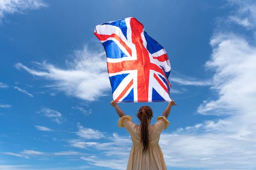 woman standing and holding UK flag under blue sky.