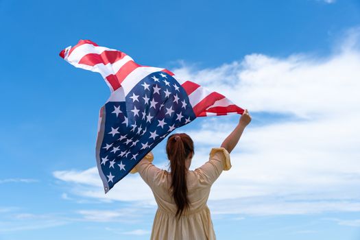 woman standing and holding USA flag under blue sky.