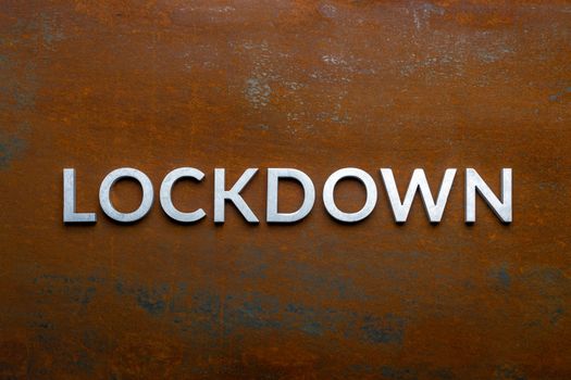 the word lockdown laid with silver metal letters on flat rusted sheet steel background in directly above perspective.