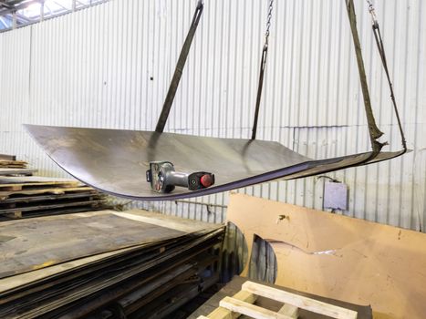 a stack of sheet metal hanging from tearing slings with crane remote control device.