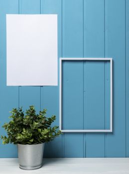 one blank black frame and a plant pot on the table with a blue wood background