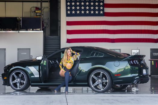 A gorgeous blonde model poses with an American muscle car inside an aircraft hangar