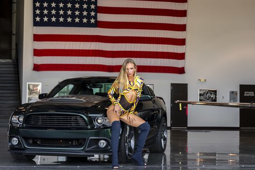 A gorgeous blonde model poses with an American muscle car inside an aircraft hangar