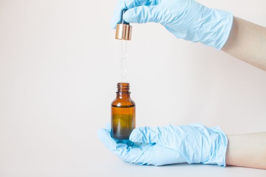 Bottles with serum for the face in his hands in protective medical rubber gloves on a light background. Beauty industry.