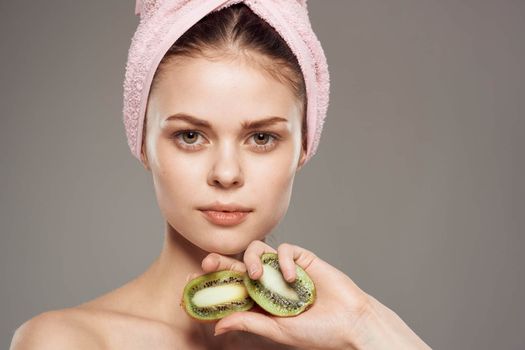 woman with pink towel on her head bare shoulders cropped view of kiwi fruit in health hand. High quality photo