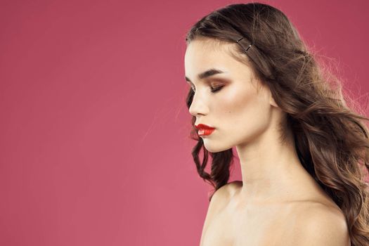 Beautiful brunette woman with makeup on her face on a pink background naked shoulders. High quality photo