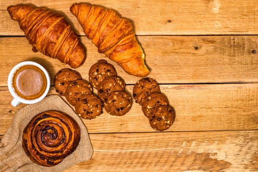 Fresh croissant and biscuits on wooden table. Coffee, food and breakfast concept. Desserts, fresh pastries and coffee. Top view and copy space