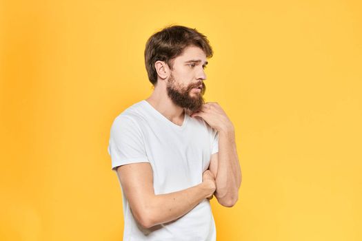 Bearded man in a white T-shirt gestures with his hands emotions studio yellow background. High quality photo