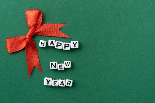 New Year concept - inscription "Happy New Year" on plastic blocks and a red Christmas bow. On a green background. Mockup for a postcard. Template for design. Copy space. Flat lay.