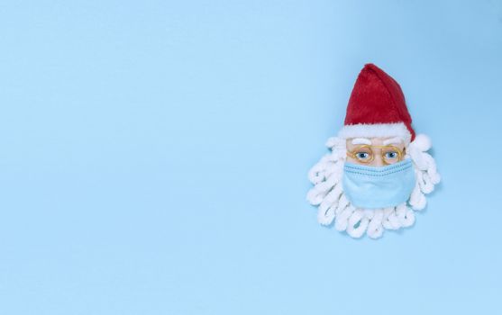 Santa Claus in medical mask on blue paper. Simple flat lay with copy space.