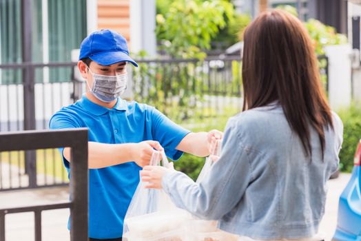 Asian young delivery man wear face mask he making grocery service giving rice food boxes plastic bags to woman customer receiving door at house after pandemic coronavirus, Back to new normal concept