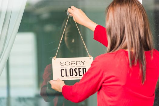 Asian young woman notice sign wood board label "SORRY WE ARE CLOSED PLEASE COME BACK AGAIN" hanging through glass door front shop, Business close during coronavirus pandemic disease concept