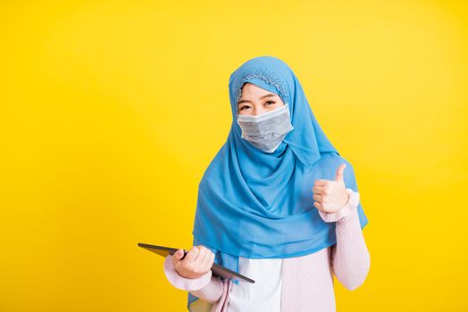 Asian Muslim Arab, Portrait of happy beautiful young woman Islam religious wear veil hijab and face mask protect she quarantines disease coronavirus show finger thumb up for good sign isolated yellow