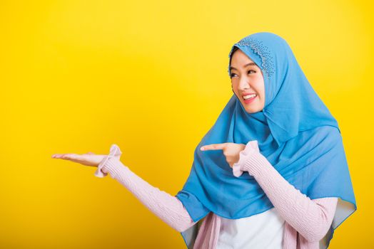 Asian Muslim Arab, Portrait of happy beautiful young woman Islam religious wear veil hijab funny smile she positive expression pointing finger side sideways to space isolated yellow background