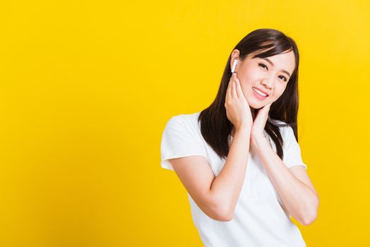 Portrait Asian of a happy beautiful young woman wear wireless earphone listening to music from smartphone having fun and dancing to sounds of favorite music studio shot isolated on yellow background