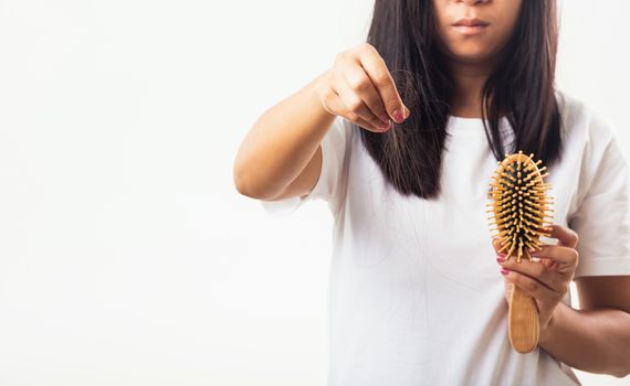 Asian woman unhappy weak hair problem her hold hairbrush with damaged long loss hair in the comb brush she pulls loss hair from the brush, isolated on white background, Medicine health care concept