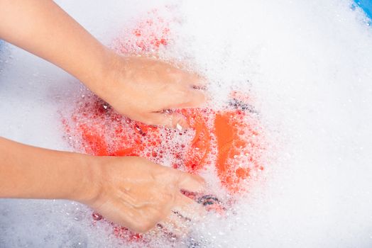 Closeup young Asian woman use hands washing color clothes in basin with detergent have soapy bubble water, studio shot background, laundry concept