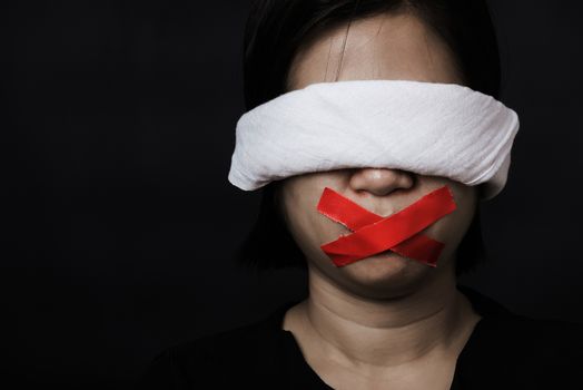 Slave Asian woman blindfold wrapping mouth with red adhesive tape, tied with chains and closed her eyes black background. Freedom speech censorship and stop talk, International Human Rights day