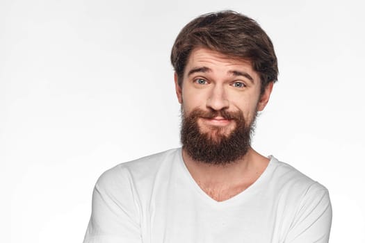 cheerful bearded man in a white t-shirt emotions gestures with his hands light background studio. High quality photo