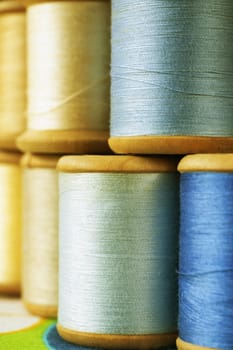 Different wooden spools of colored thread on  colored background , different shades of blue and yellow color  in every spool