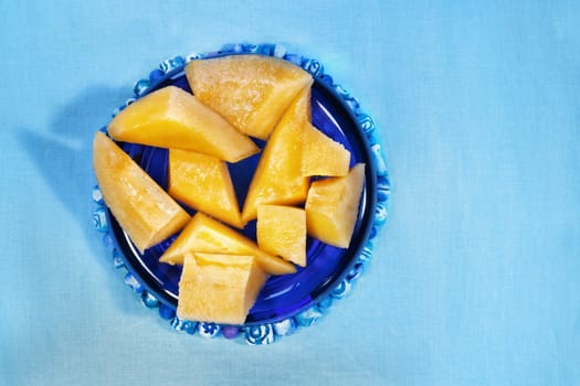 Several pieces of orange muskmelon on blue background , fruit pieces are in a blue bowl