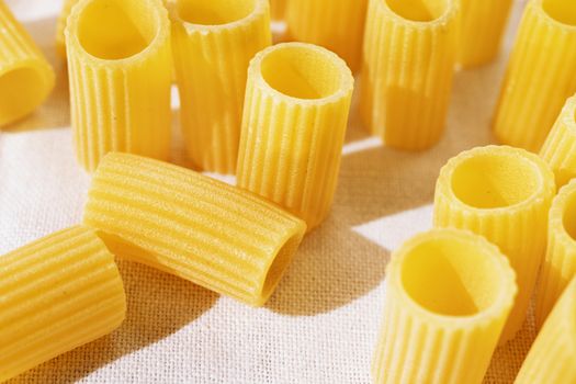 Italian pasta called mezzi rigatoni on white cotton cloth ,tube-shaped pasta with ridges down their lenght ,studio shot