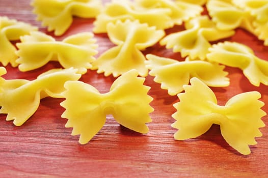 Dry italian pasta called farfalle on wooden red table , beautiful bow tie  -shape pasta