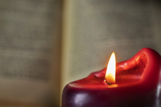 Reading under lighted candle , in the foreground one red candle ,in the background an opened book out of focus