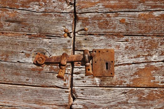 Old vintage rusty iron latch on cracking door ,the door is made  of horizontal wooden boards brown painted 