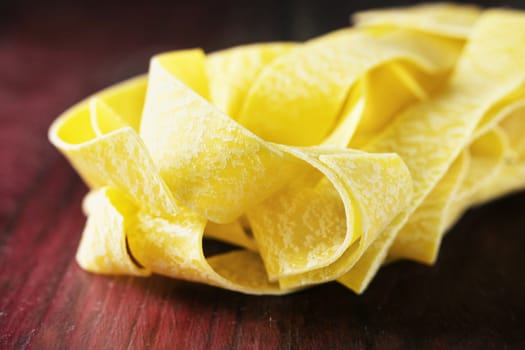 Dry pasta pappardelle on wooden table ,delicious yellow  large flat pasta noodles 