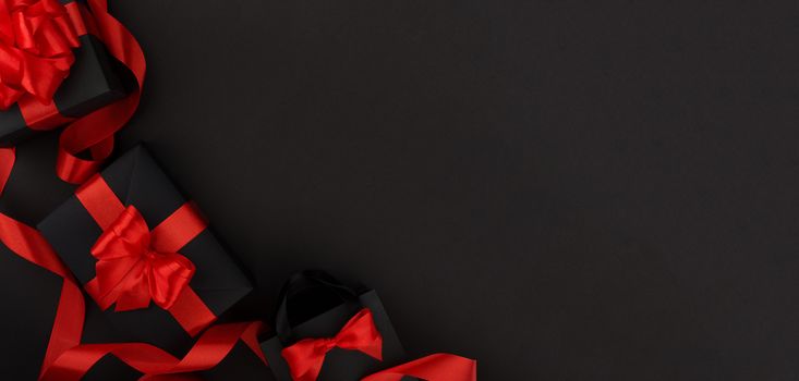 Gift box wrapped in black paper with red ribbon on black background, design banner black friday sale concept copy space for text
