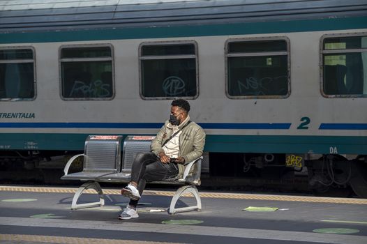 terni,italy november 03 2020:black boy waits for the train with medical mask due to corona virus