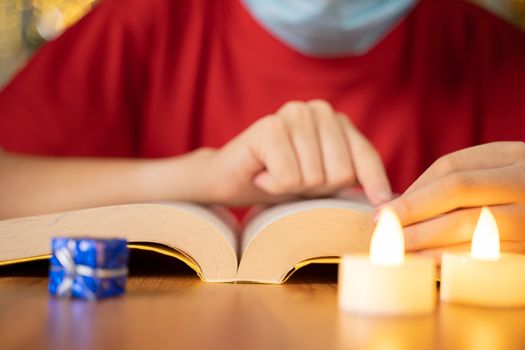 Close up shot of hands reading bible with candles in front on decorated Christmas background during xmas festival celebration.