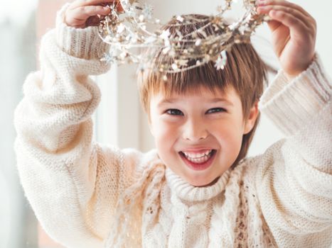 Kid with decorative star tinsel for Christmas tree. Boy in cable-knit oversized sweater. Cozy outfit for snuggle weather. Winter holiday spirit.New year.