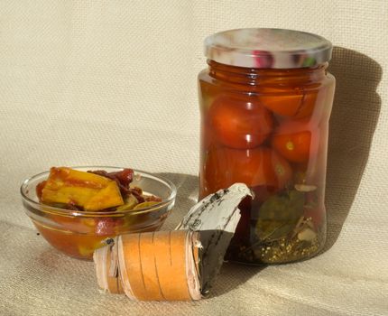 A jar of pickled tomatoes, a bowl of pickled hot peppers on a background of flax and birch bark