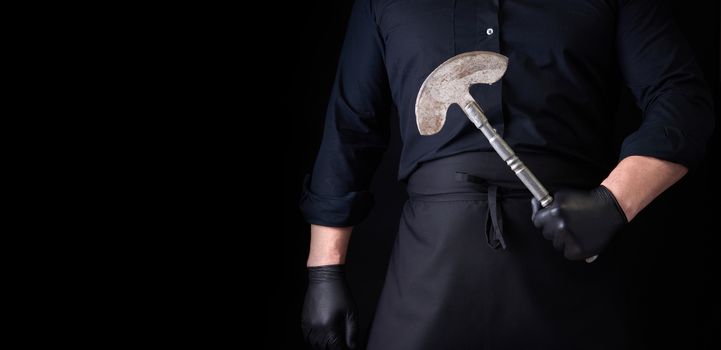 man in black clothes, latex gloves holds a vintage metal ax-knife for meat and vegetables, dark background, copy space