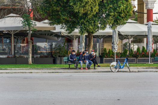 Unidentified crowd with face protection on a bench as Hellenic government orders lockdown to prevent COVID-19 spread.