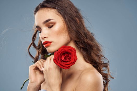 Portrait of a woman with a red rose in her hands on a gray background naked shoulders evening makeup. High quality photo