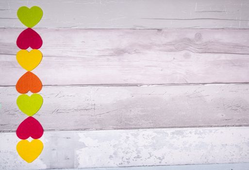 Colorful felt hearts on a background of old wooden planks resembling an old parquet floor. Concept of valentine's day and love in general.